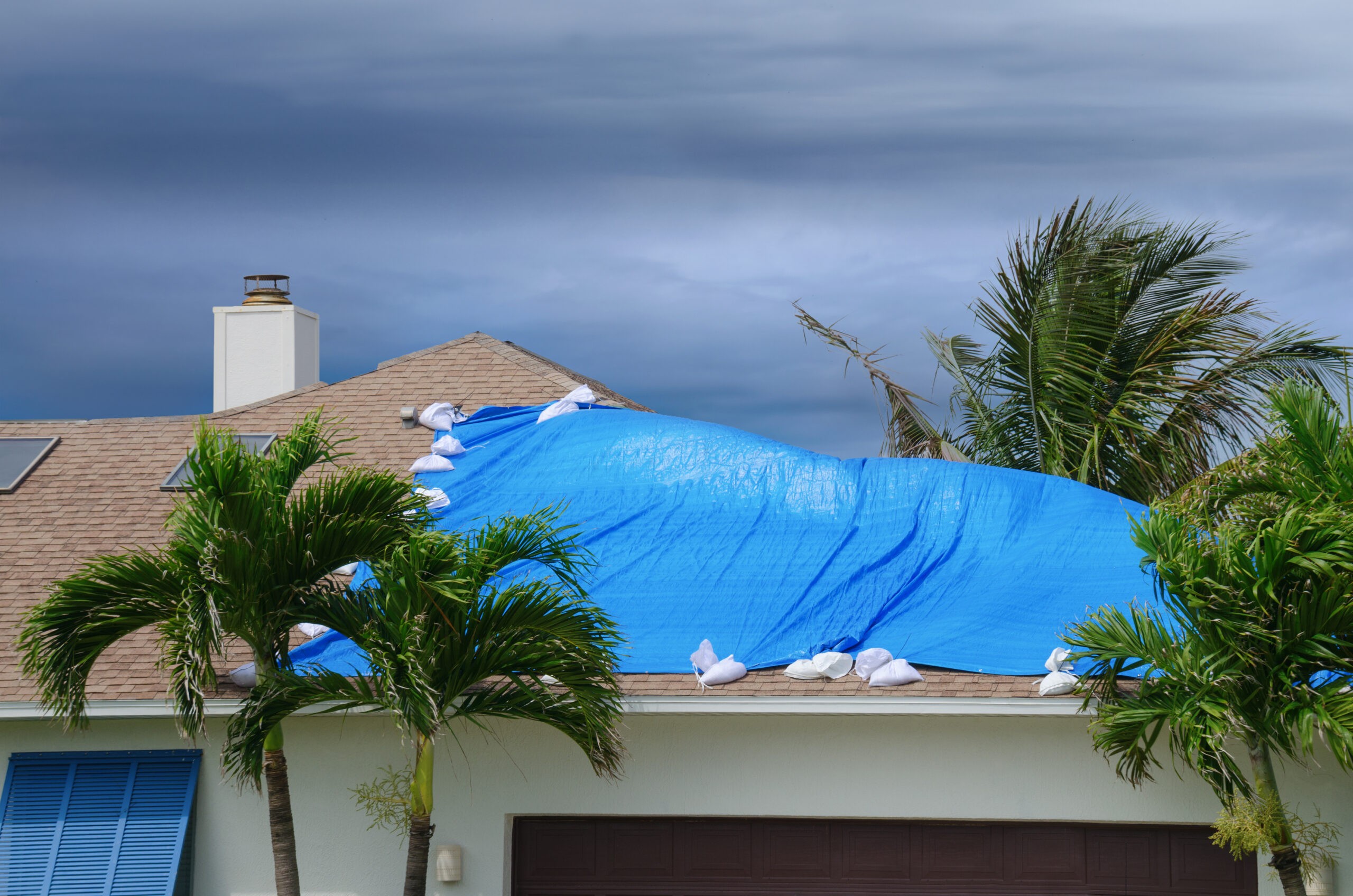 hurricane-prone damaged roof on house with a blue plastic tarp over hole